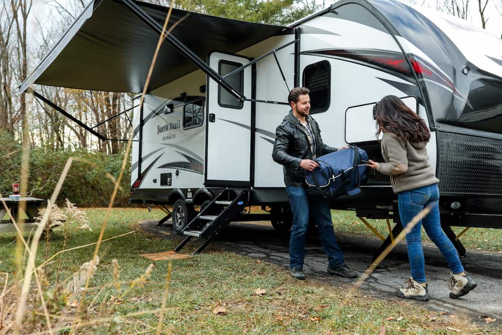 Learning to winterize your campers is important. a man and a woman are putting a bag in a camper