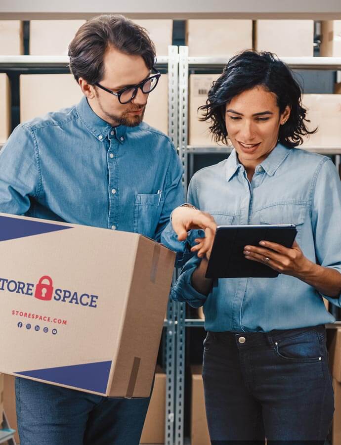A man holding a moving box is pointing on a tablet a woman holds.