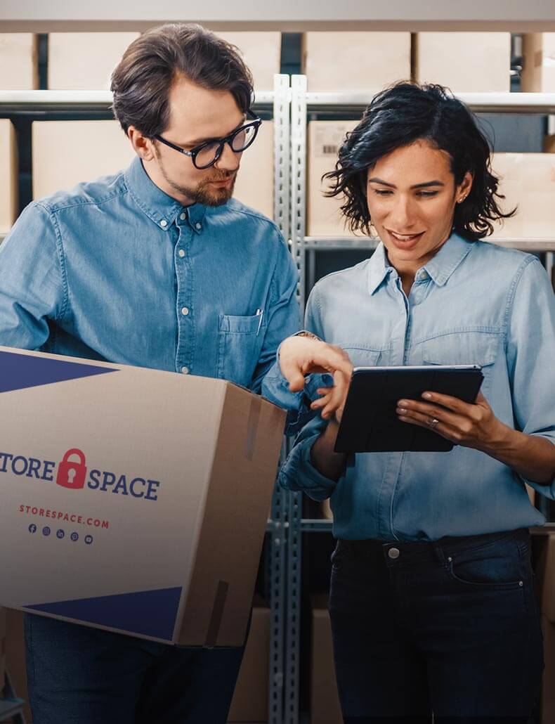A man holding a moving box is pointing on a tablet a woman holds.
